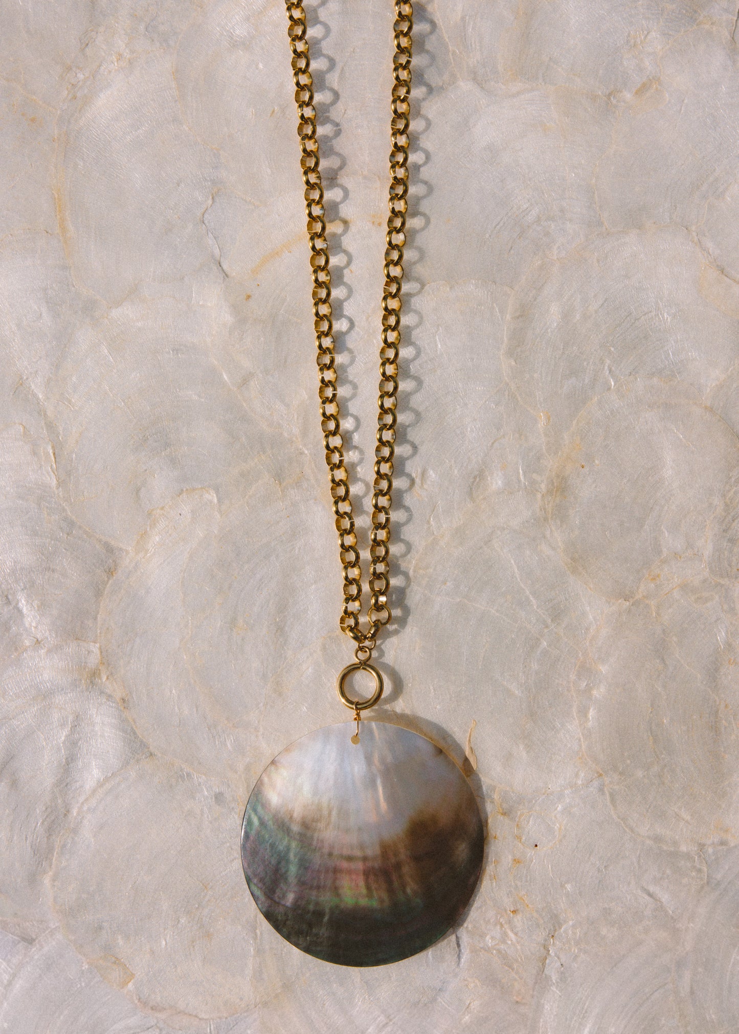 A gold-tone chain necklace with a large, round pendant, displayed against a textured, light-colored stone background.