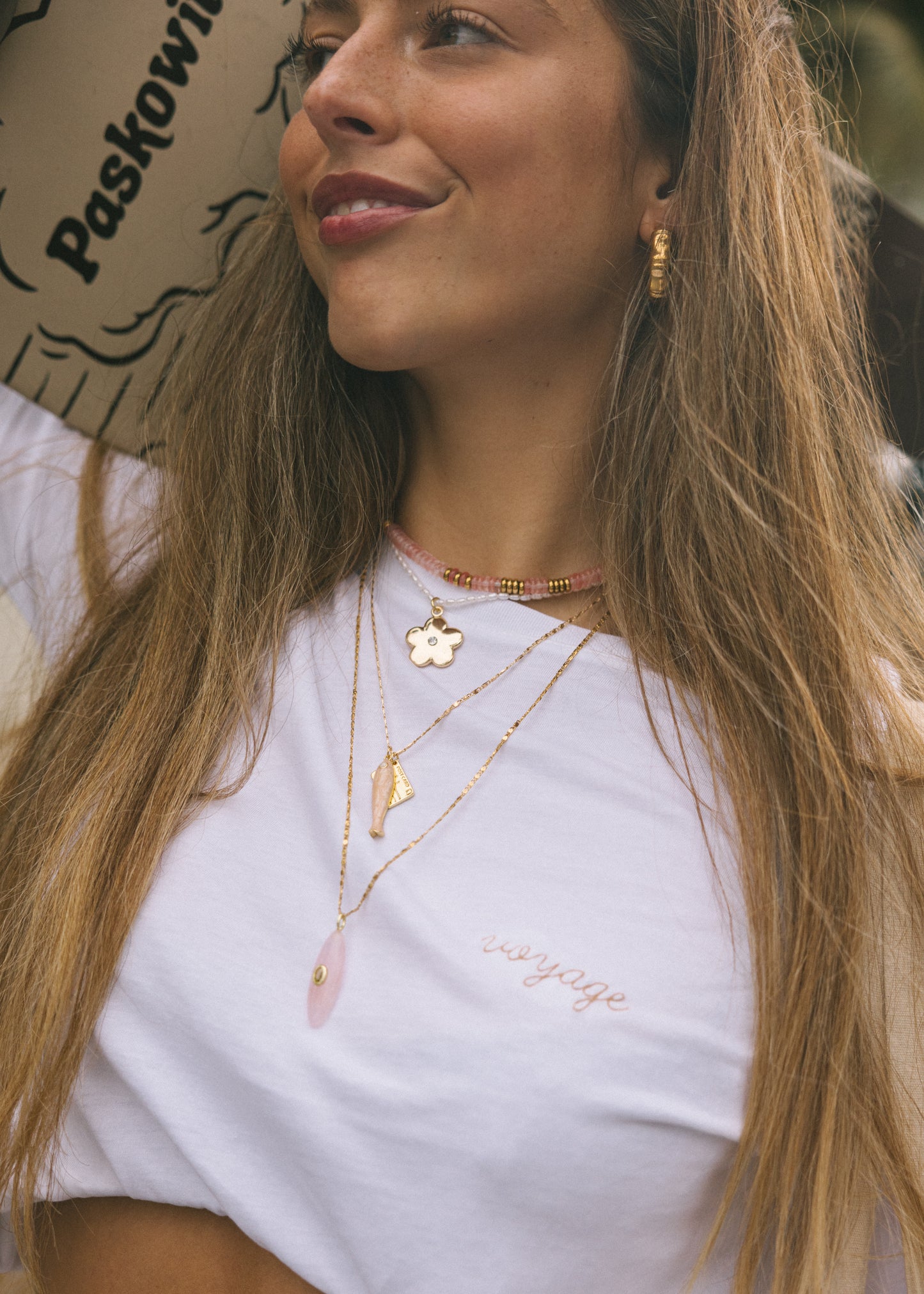 Woman wearing gold necklaces with a white top outdoors