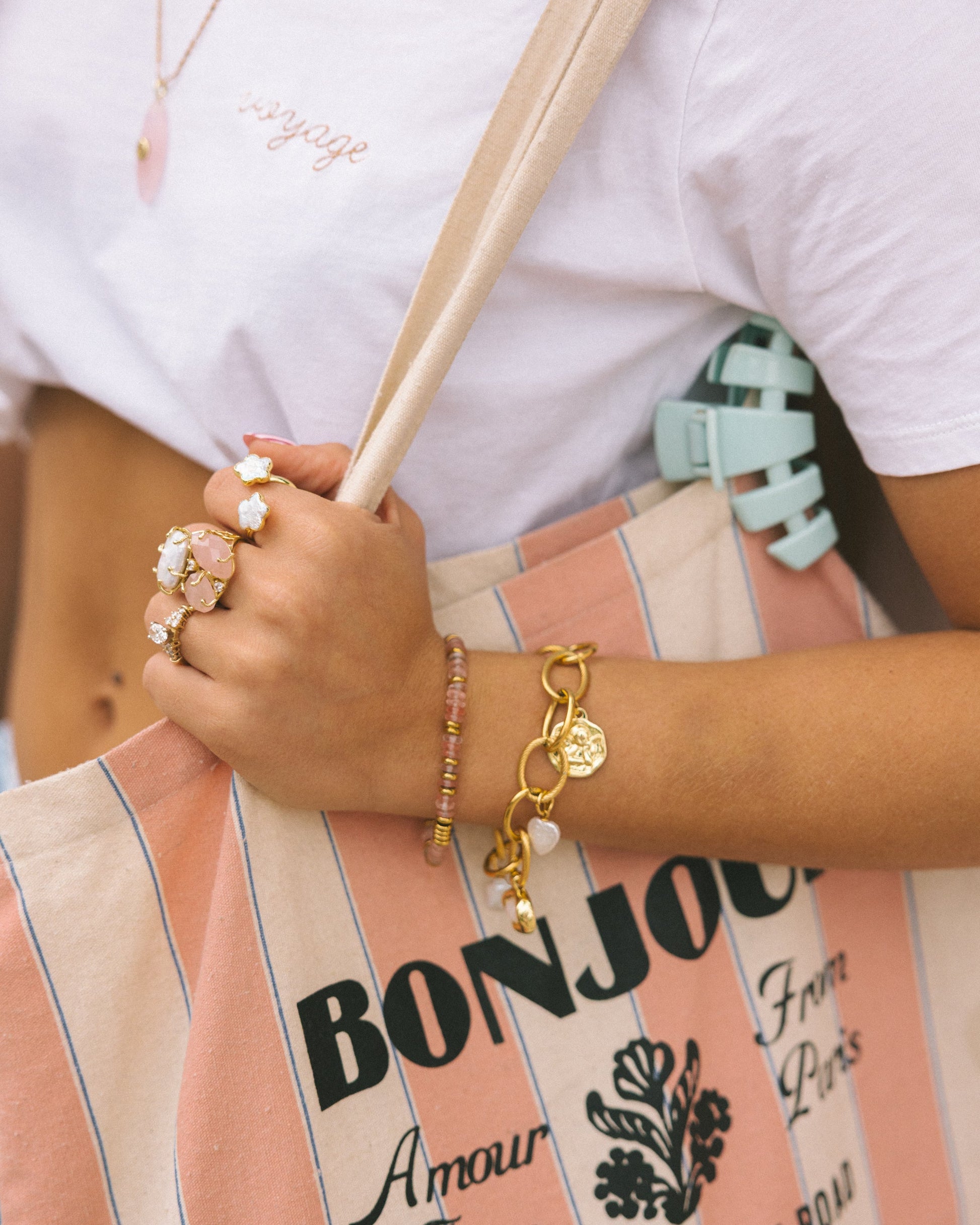 Person holding a striped bag with 'Bonjour' text, wearing jewelry.