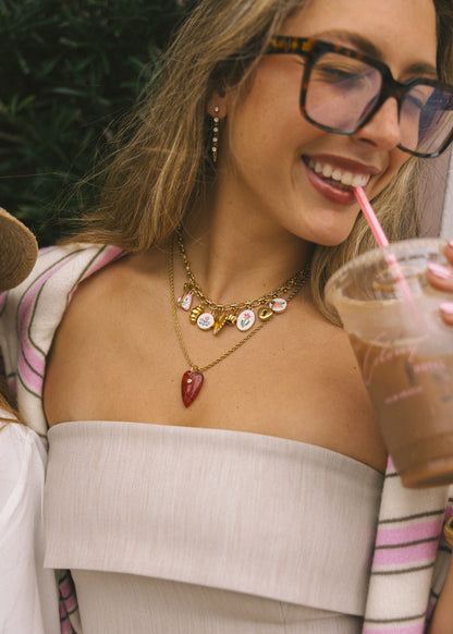 Woman with glasses holding a drink, wearing a necklace with multiple pendants.