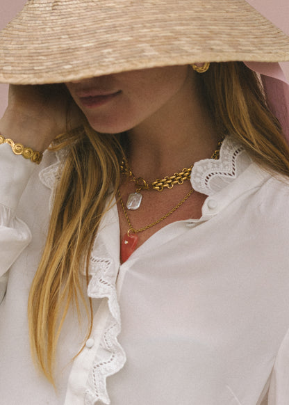Person wearing a straw hat, white blouse with ruffled details, and gold jewelry.