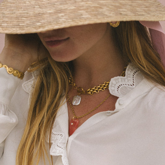 Person wearing a straw hat, white blouse with ruffled details, and gold jewelry.