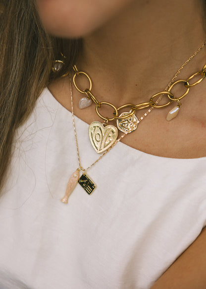 Gold necklace with heart and key charms worn by a person against a white background