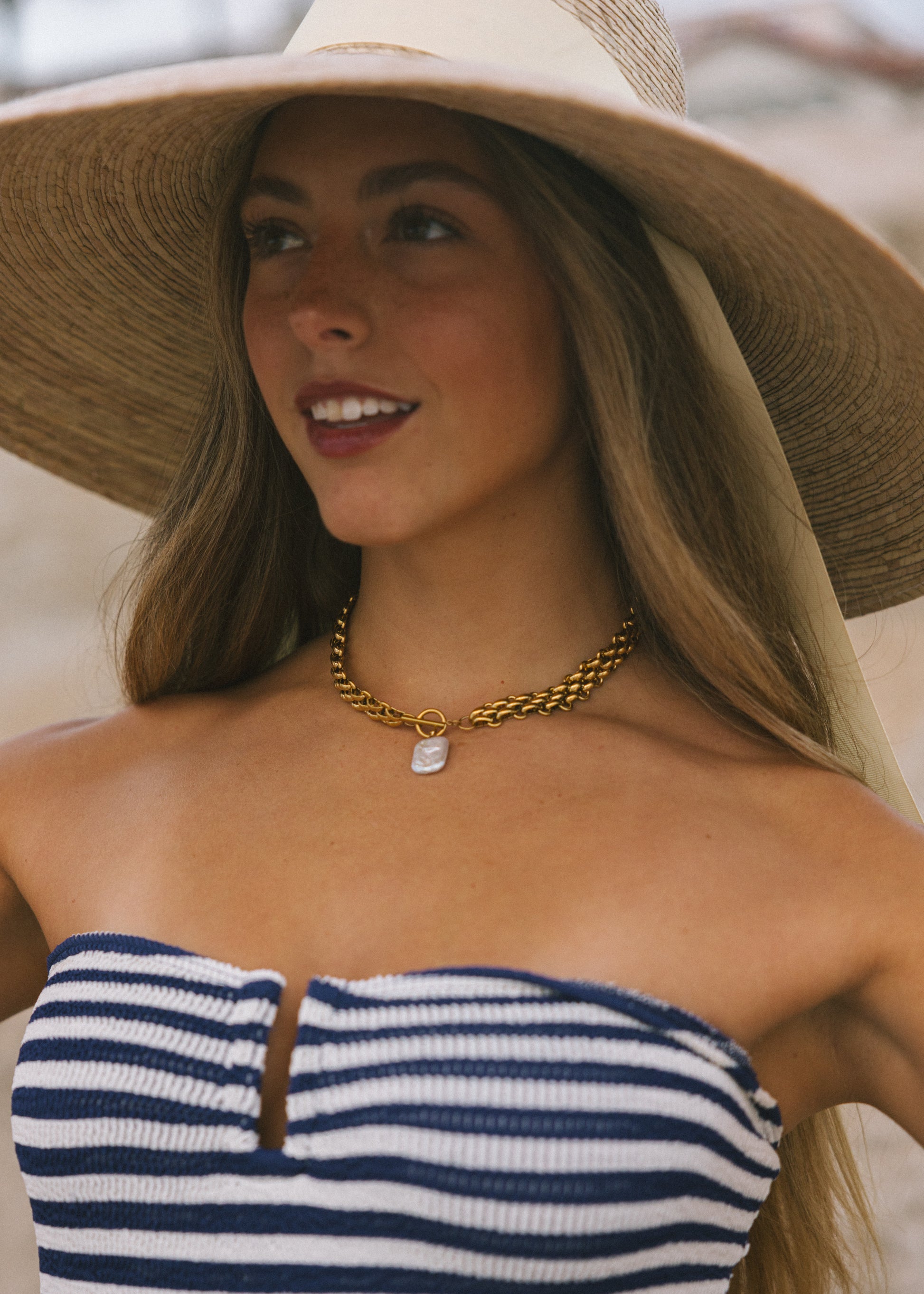 Woman wearing a wide-brimmed hat and striped top, smiling outdoors.