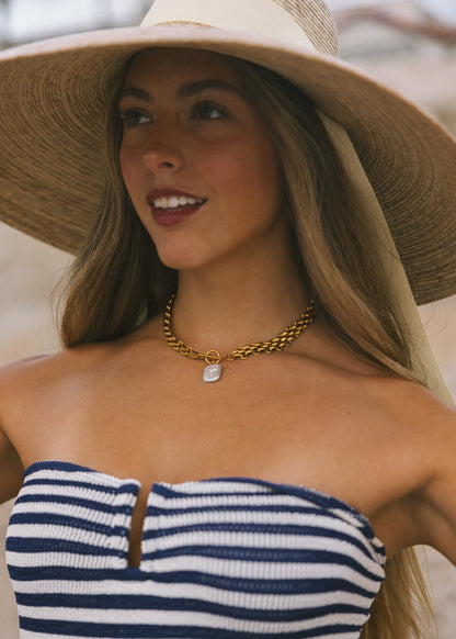 Woman wearing a wide-brimmed hat and striped top, smiling outdoors.