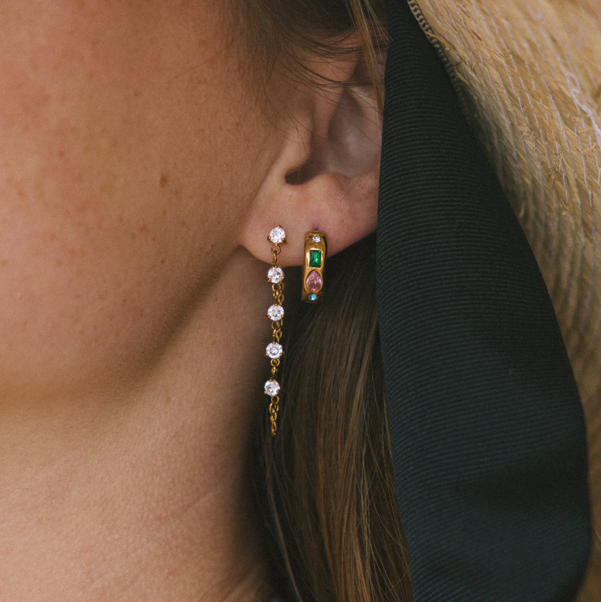 Close-up of a person wearing gold hoop earrings with gemstones.