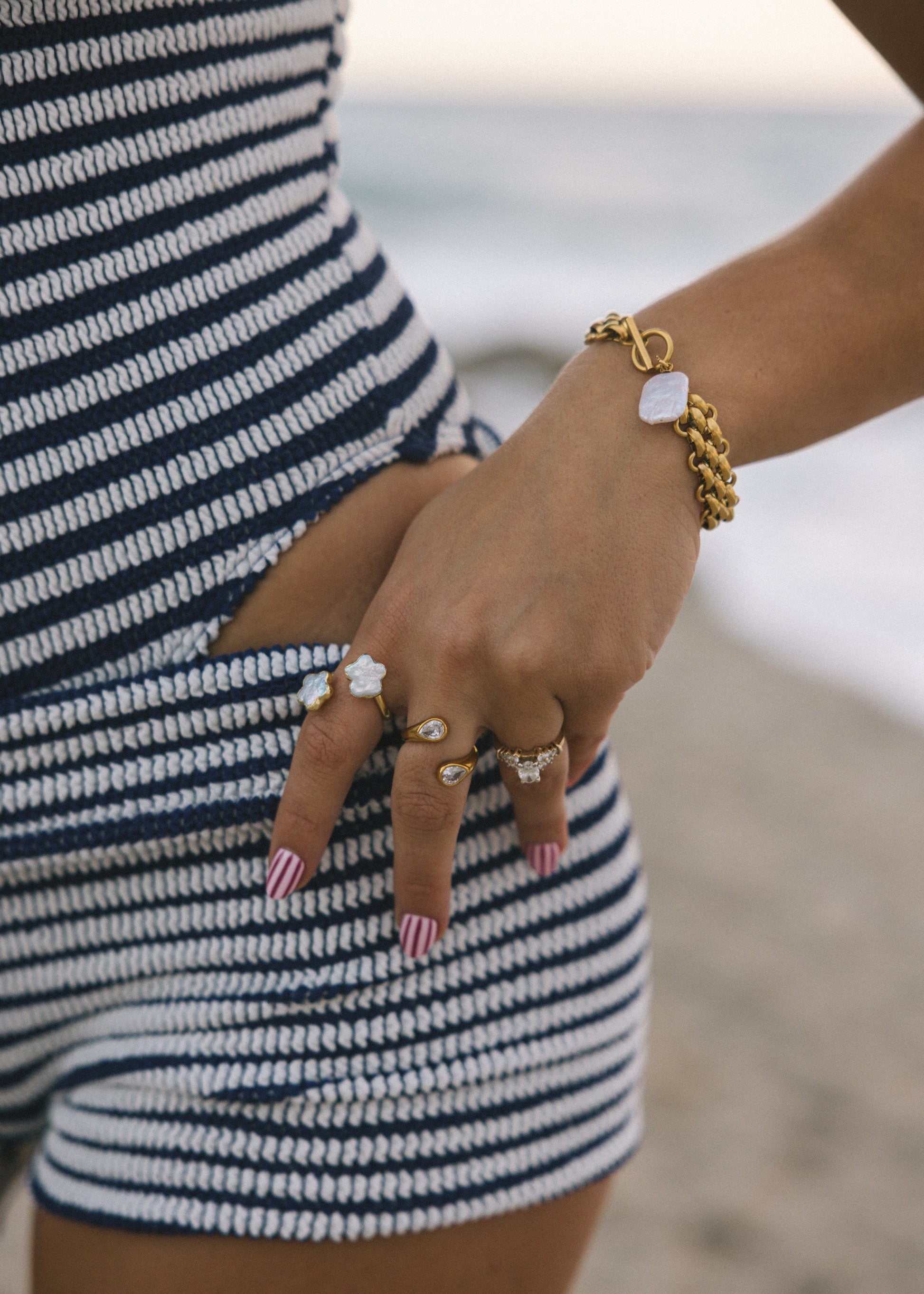Person wearing a gold bracelet and rings with a blurred beach background