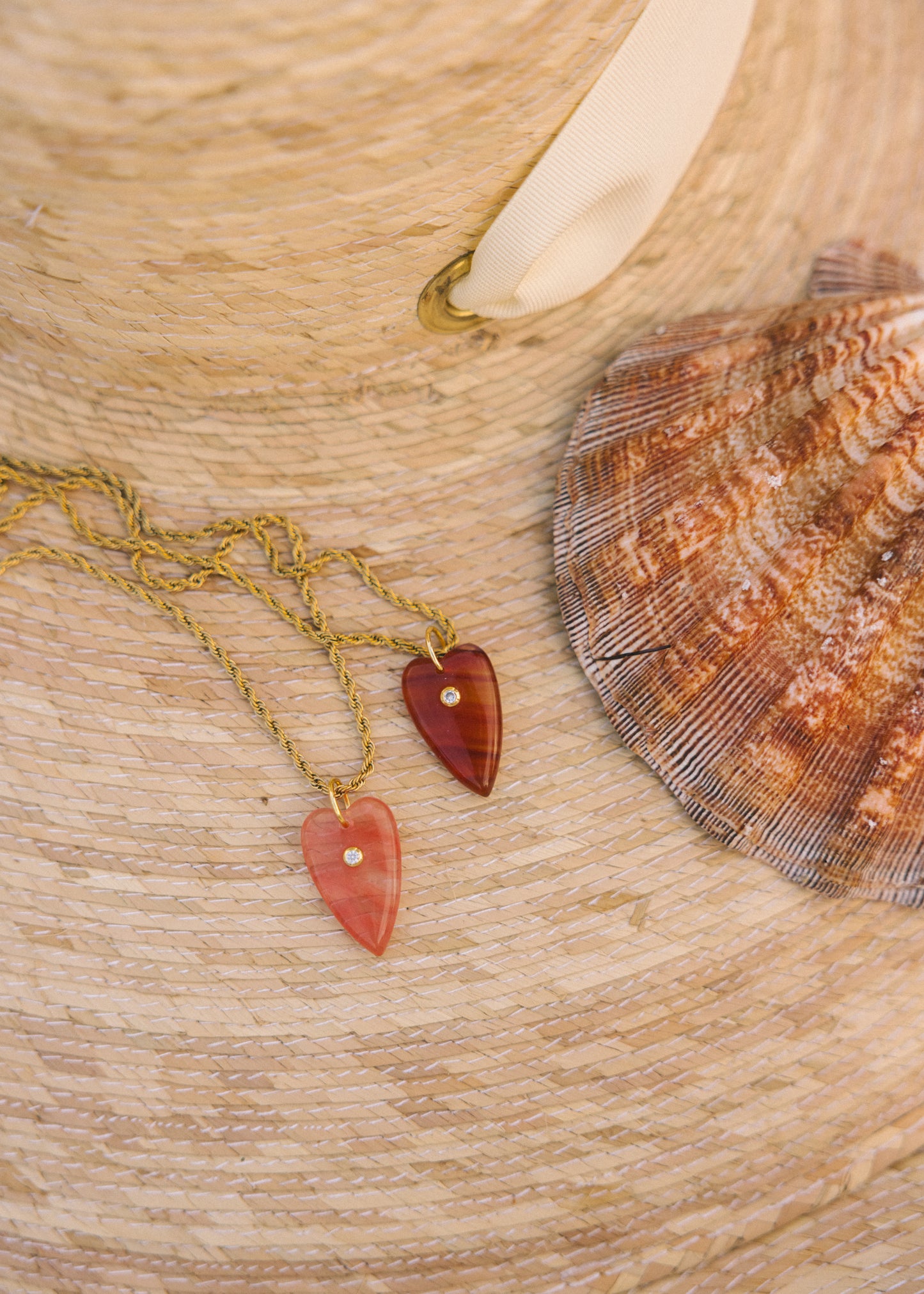 Two heart-shaped pendants on gold chains with a shell in the background on a wooden surface