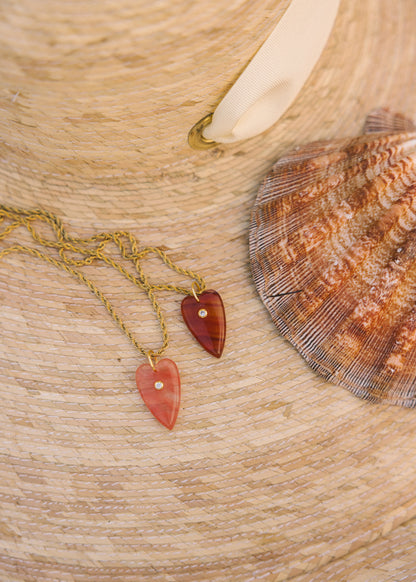 Two heart-shaped pendants on gold chains with a shell in the background on a wooden surface