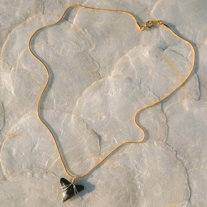 Gold necklace with a black pendant on a textured stone surface